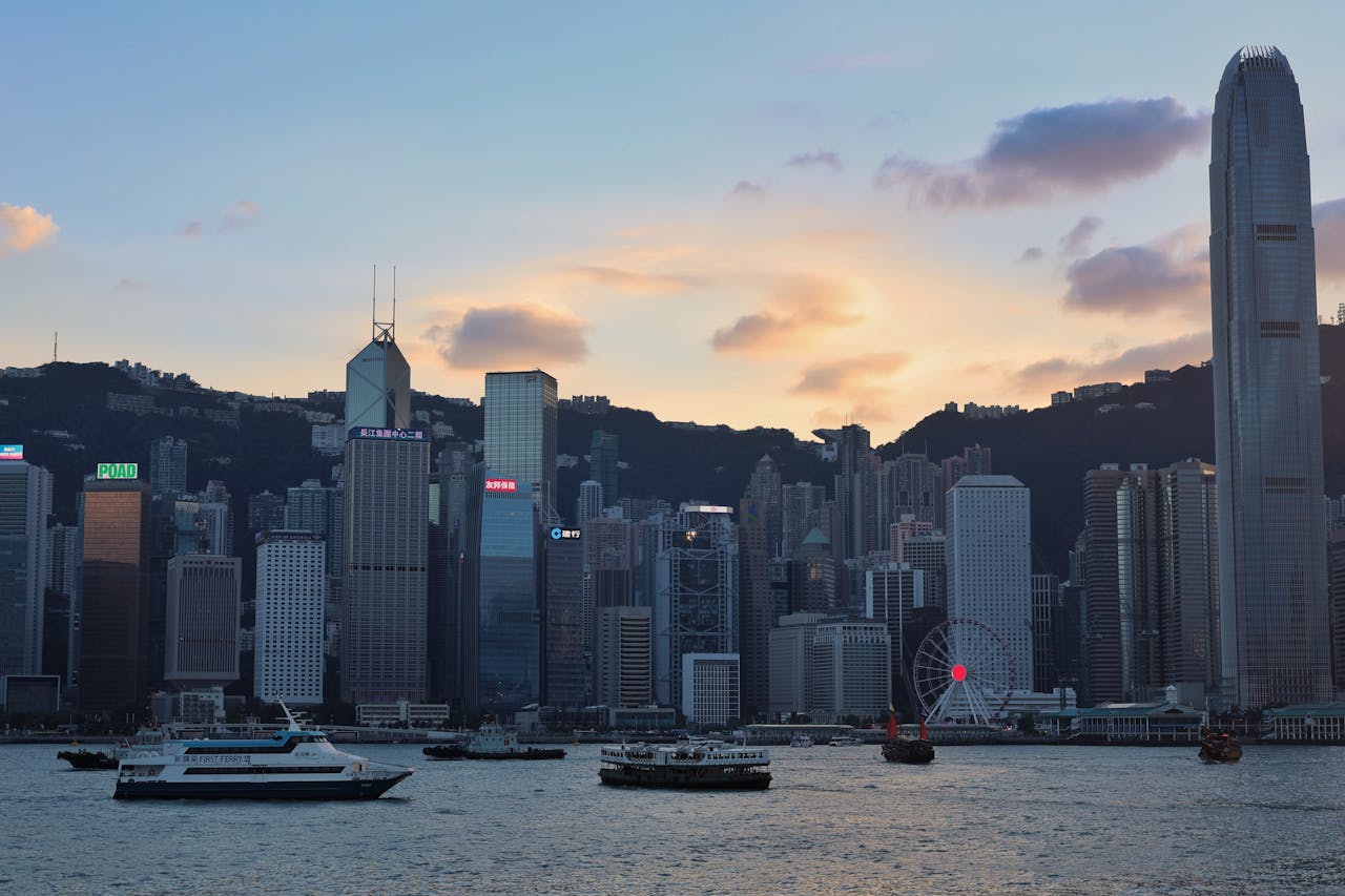 Stunning view of Hong Kong skyline at sunset, showcasing ferries on the water and iconic skyscrapers.
